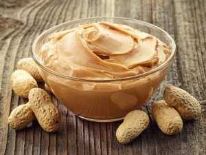 Bowl of peanut butter sitting on a wood surface with peanuts in shells around it