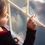 yound girl drawing a heart on a fogged windo
