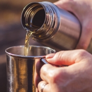 Man’s hands pouring liquid from a thermos into a metal cup Man's hands pouring liquid from a thermos into a metal cup